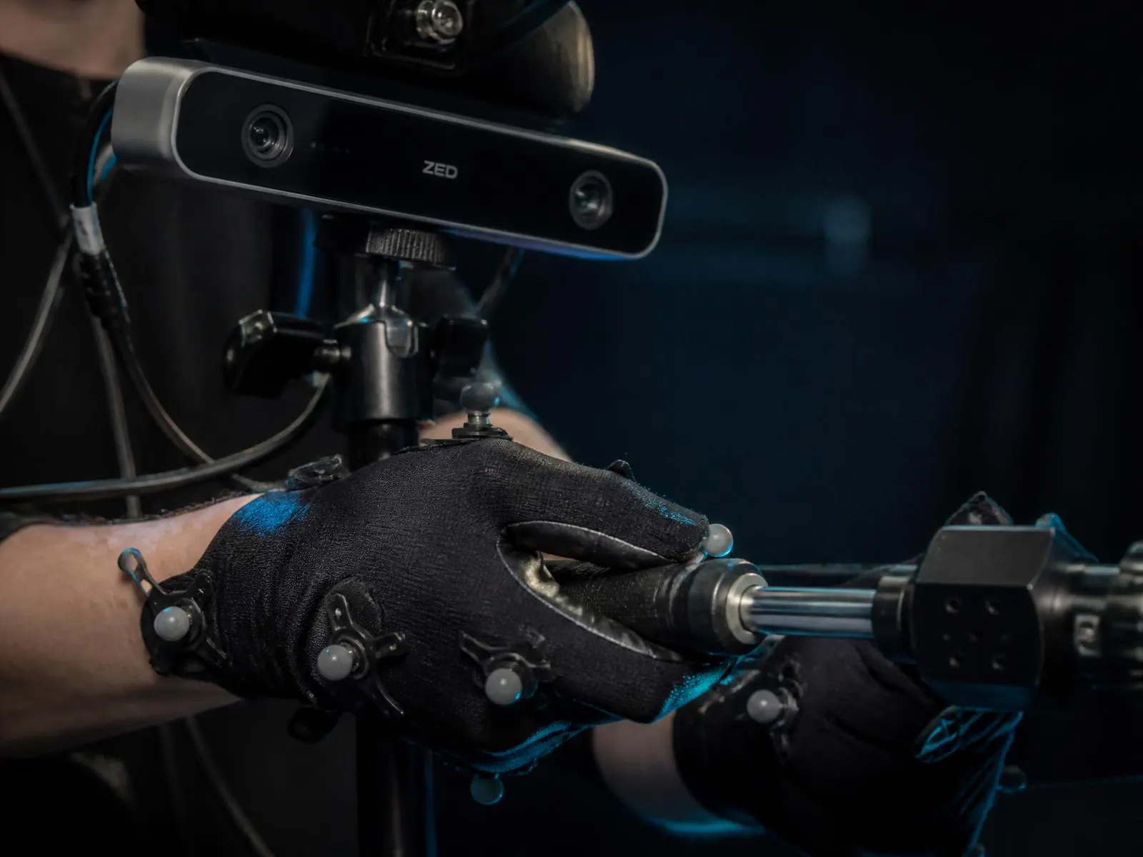 Hands in motion-capture gloves with a stereo depth camera rig grasping a tool